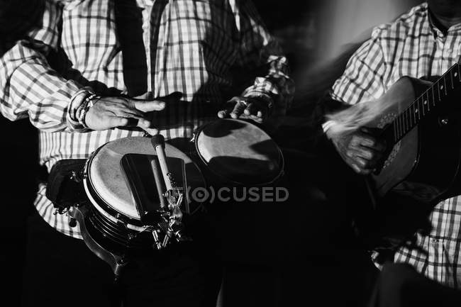 Cropped of male musicians playing drums and guitar in night club, black and white shot with long exposure — Stock Photo