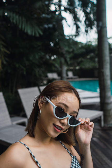 Retrato de jovem mulher em óculos de sol elegantes na piscina — Fotografia de Stock