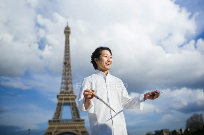 Sorridente chef japonês com facas em pé em frente à Torre Eiffel em Paris — Fotografia de Stock
