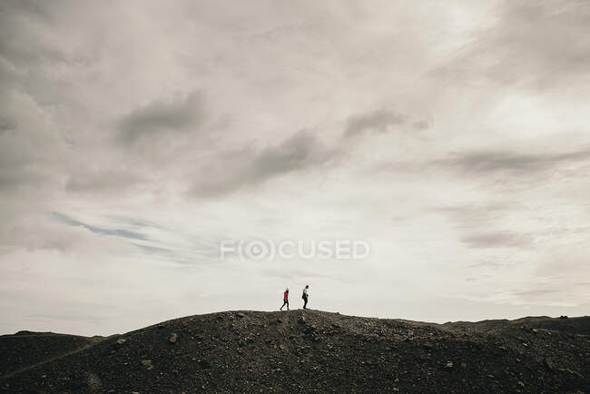 Vue latérale de touristes méconnaissables marchant sur une colline sèche par temps nuageux. — Photo de stock