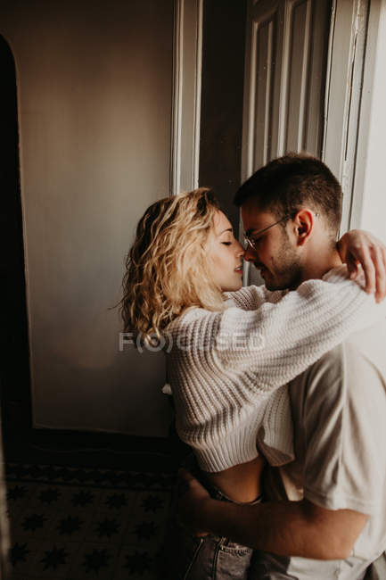 Casal afetuoso abraçando na janela em casa — Fotografia de Stock