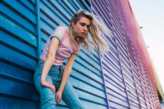 Blonde young woman leaning on blue wall on street — Stock Photo