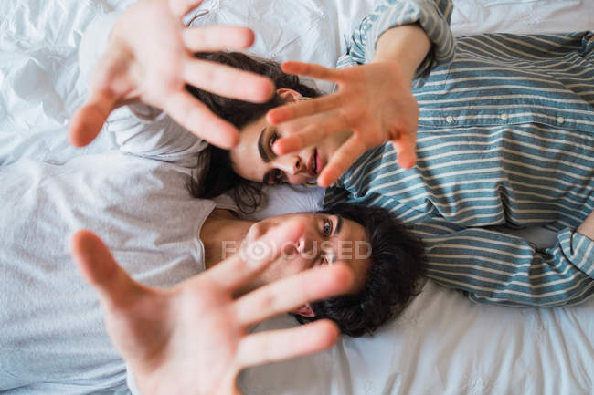 Young man and woman lying on bed and posing with hands up at home — Stock Photo