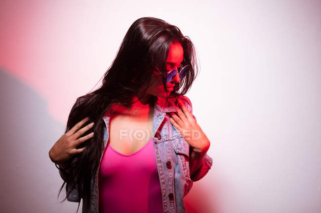 Young pink dressed woman in sunglasses standing at white wall — Stock Photo