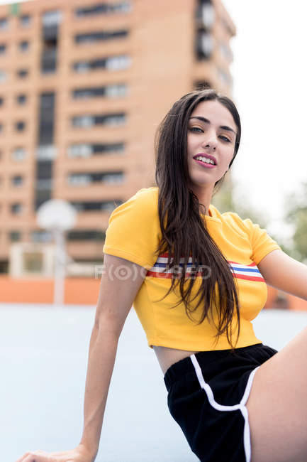 Jeune femme en vêtements de sport assis sur le sol dans la ville et regardant la caméra — Photo de stock