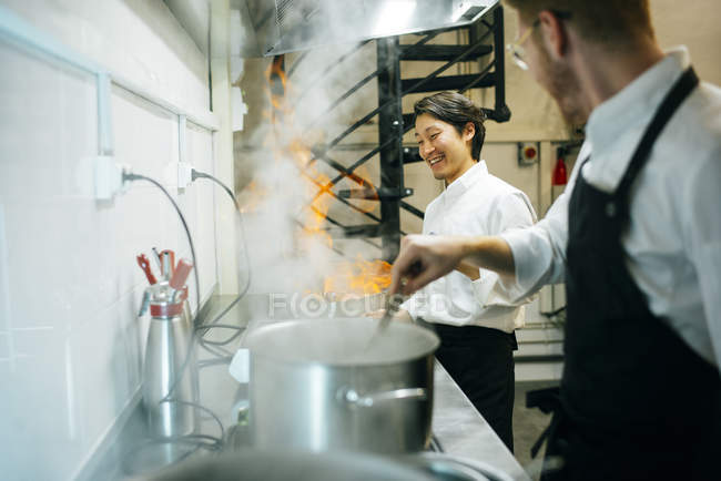 Glücklicher Koch, der in der Restaurantküche mit Kollegen Flammkuchen kocht — Stockfoto