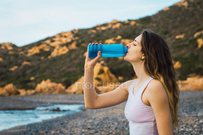 Adatto donna che beve dalla bottiglia al mare — Foto stock