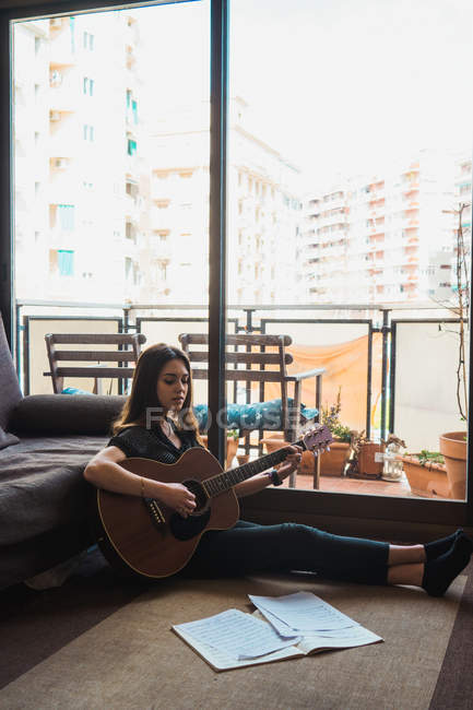 Женщина играет на гитаре, сидя дома на полу — стоковое фото