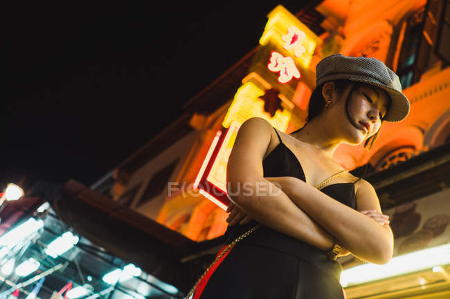 Elegante jovem mulher asiática bonita de pé na rua iluminada à noite com os olhos fechados — Fotografia de Stock