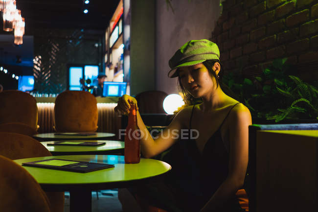 Elegante jovem mulher asiática sentada no café e tendo garrafa de bebida — Fotografia de Stock
