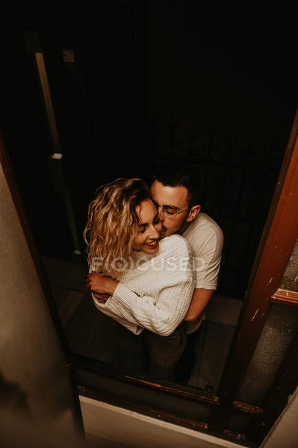 Alegre hombre y mujer de pie y abrazándose en la ventana en casa - foto de stock