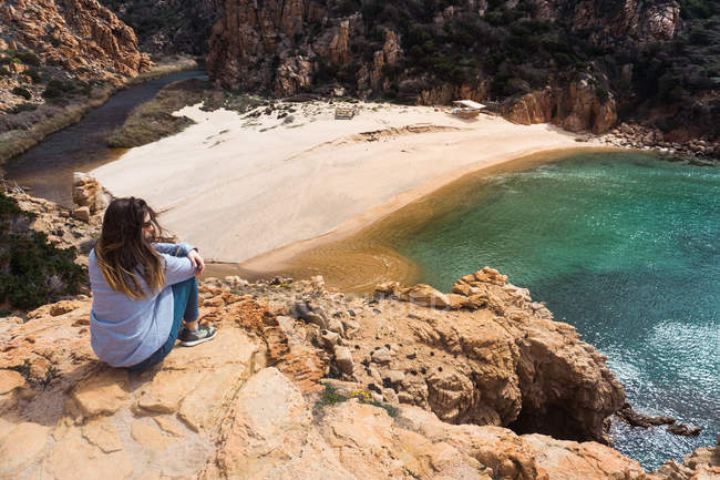 Жінка сидить на скелях на узбережжі і дивиться на — стокове фото
