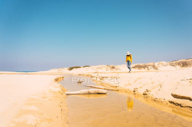 Frau mit Hut steht am sandigen Ufer unter blauem Himmel — Stockfoto