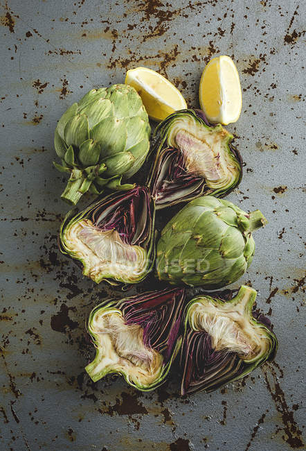 Fresh halved artichokes and pieces of lemon on grunge background — Stock Photo