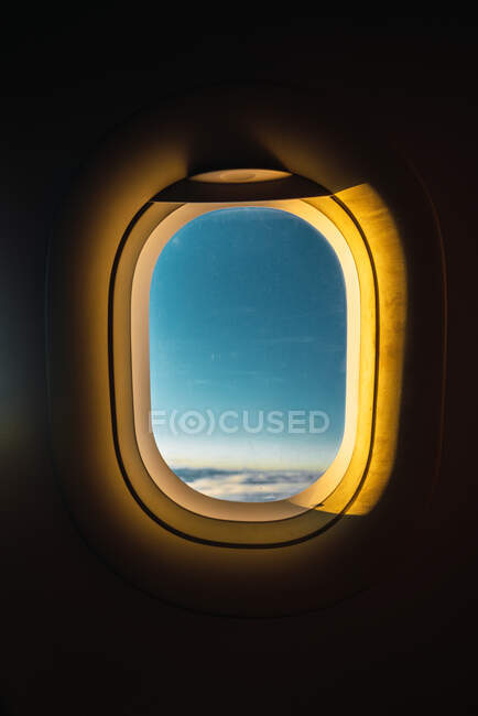 Shot from inside of airplane window with blue sky behind illuminated with golden lights of sunset — Stock Photo