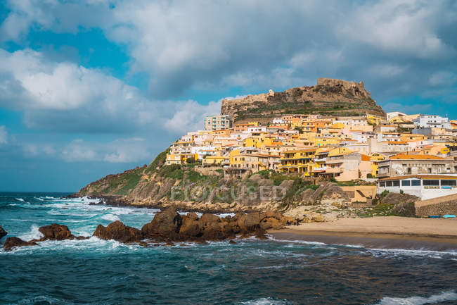 Pequeña ciudad con edificios coloridos en la colina rocosa en la costa, Cerdeña, Italia - foto de stock