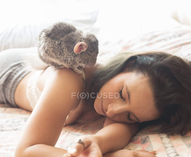 Young woman lying in bed with chinchilla on shoulder — Stock Photo