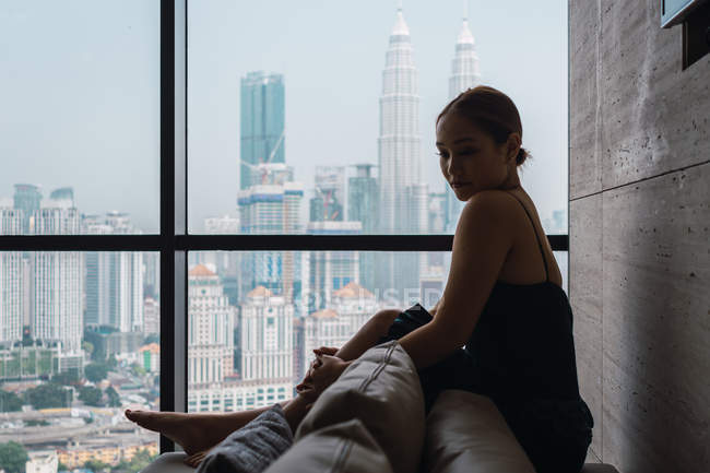 Pretty woman relaxing in armchair in apartment with city view — Stock Photo