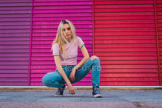 Femme blonde confiante assise sur des nichons contre un mur multicolore — Photo de stock