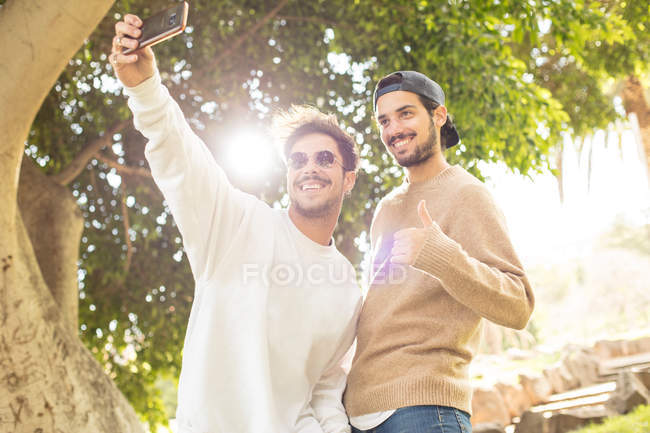 Sorrir felizes amigos do sexo masculino tomando selfie com smartphone no parque ensolarado — Fotografia de Stock