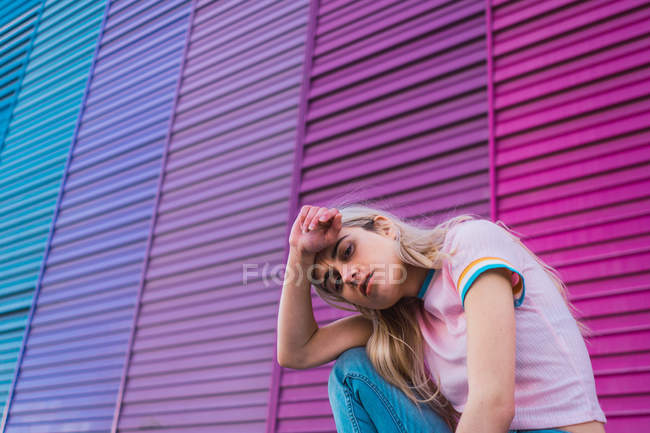 Joven mujer rubia sentada contra la pared multicolor - foto de stock