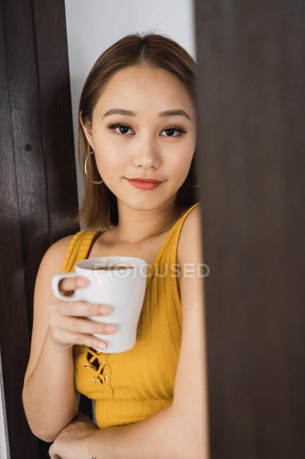 Portrait of young asian woman with cup leaning on wall — Stock Photo
