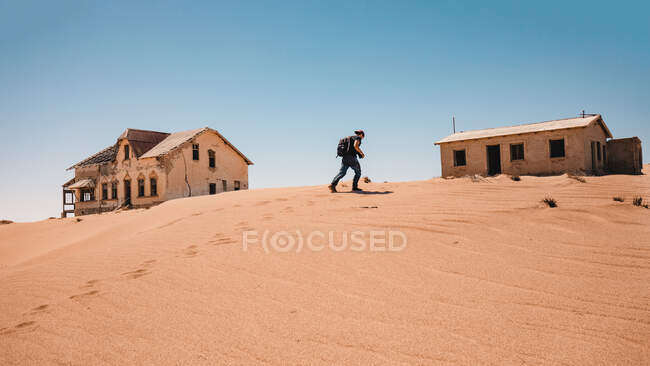 Side view of hiking person walking on sandy hill to small house in cloudless day. — Stock Photo