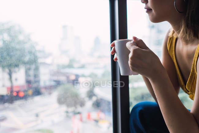 Frau hält Tasse beim Blick durchs Fenster — Stockfoto