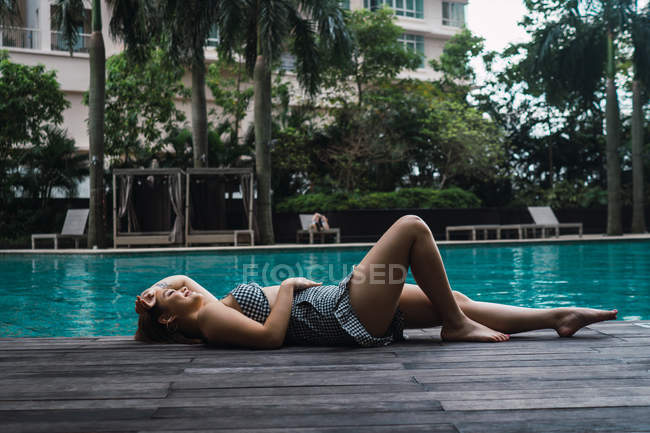 Souriant jeune femme détendue allongée à la piscine — Photo de stock