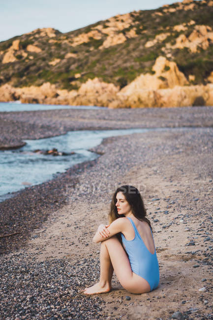 Nachdenkliche junge Frau im Badeanzug sitzt am Strand — Stockfoto