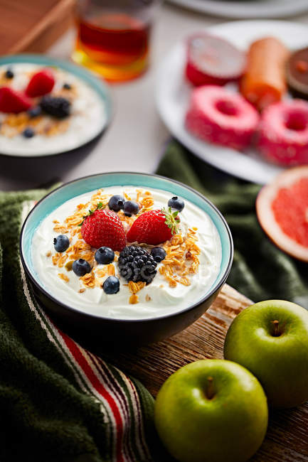 Миска свіжого йогурту з ягодами та кукурудзяними пластівцями на дошці — стокове фото