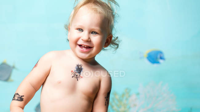 Cheerful cool toddler boy with instant tattoos smiling and looking at camera — Stock Photo