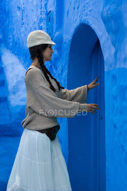 Brünette Hündin mit Zöpfen und Mütze berührt blaue Tür in Marokko — Stockfoto
