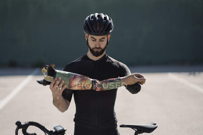 Handsome bearded man in helmet holding arm prosthesis while standing near bike — Stock Photo