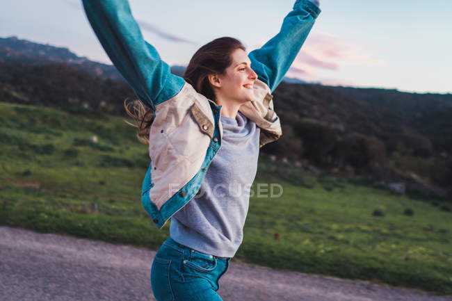 Jovem mulher alegre andando na estrada com os braços para cima na natureza — Fotografia de Stock