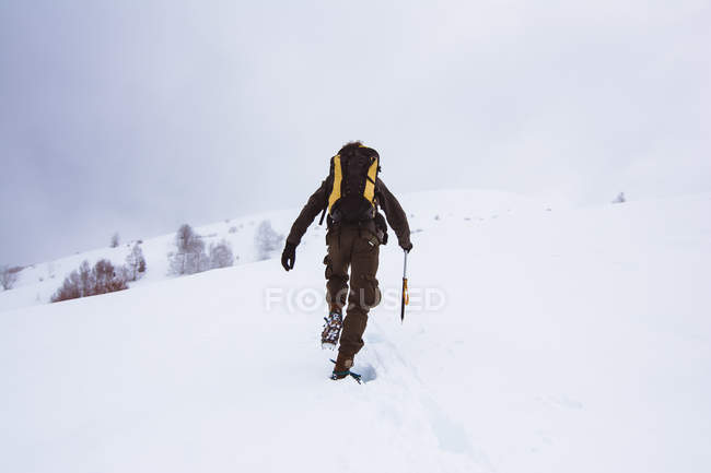Tourist mit Rucksack klettert auf verschneiten Berg — Stockfoto