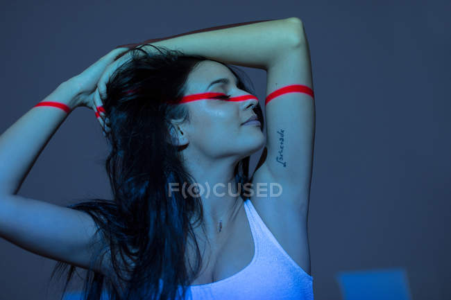 Junge attraktive Frau mit rotem Strich im Gesicht und Armen auf dunklem Hintergrund — Stockfoto