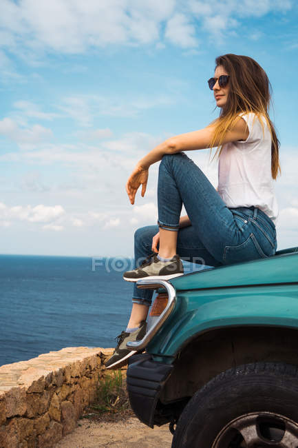 Красива жінка сидить на багажнику автомобіля і дивиться в сторону на узбережжя — стокове фото