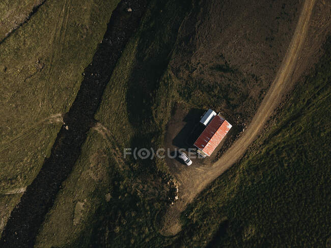 Dall'alto piccola casa e auto parcheggiata nelle vicinanze in un campo verde. — Foto stock