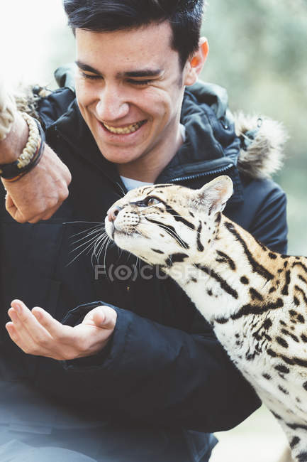 Усміхнений молодий чоловік годує леопарда в зоопарку — стокове фото