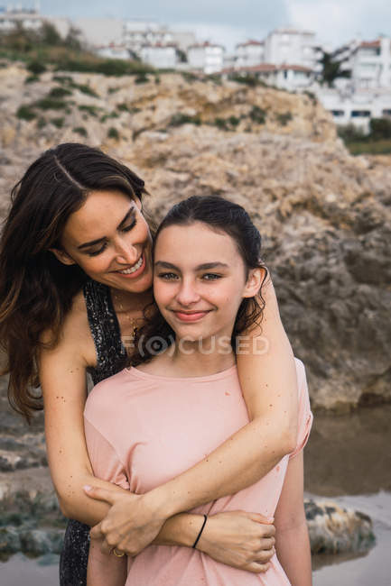 Donna che abbraccia sorridente figlia in riva al mare sfondo in estate — Foto stock
