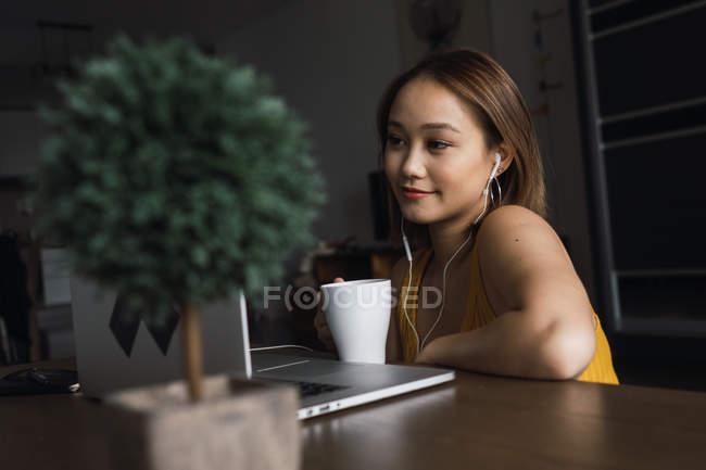 Женщина с чашкой с помощью ноутбука за столом в квартире — стоковое фото