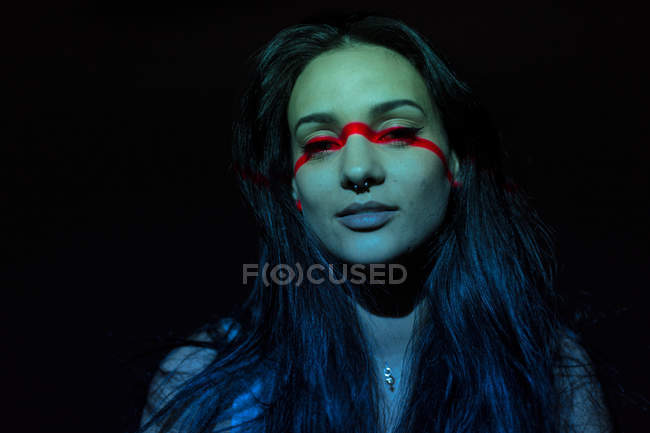 Jeune femme attrayante avec ligne rouge sur le visage en regardant la caméra sur fond noir — Photo de stock