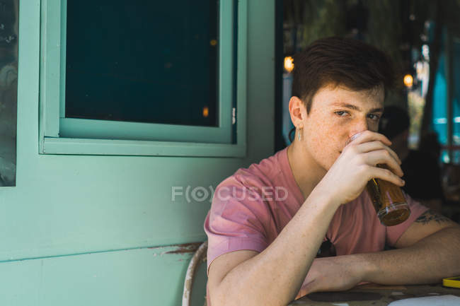 Впевнений молодий чоловік сидить зі склянкою пива за столом — стокове фото