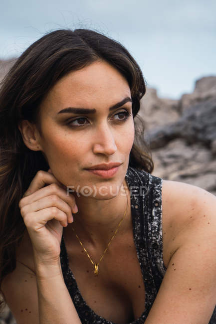 Вдумчивая женщина сидит на улице с камнем на заднем плане — стоковое фото