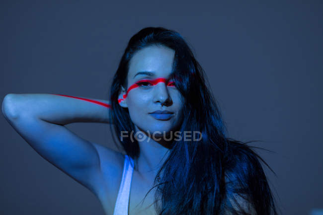 Giovane donna attraente con linea rossa sul viso e braccio guardando su sfondo scuro — Foto stock