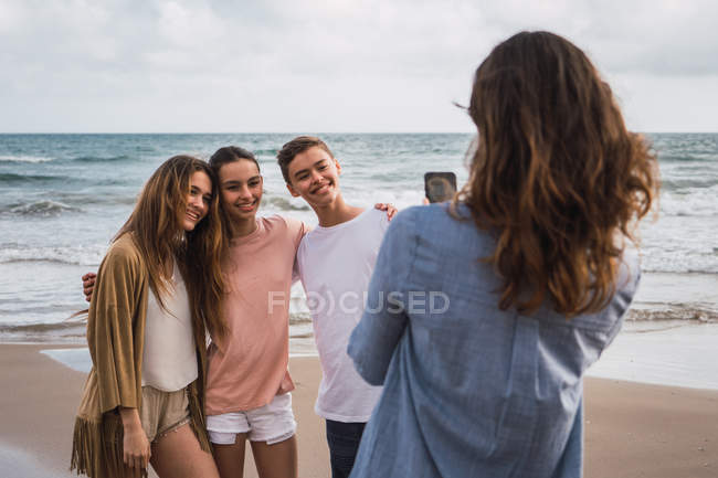 Женщина фотографирует детей со смартфоном на пляже — стоковое фото