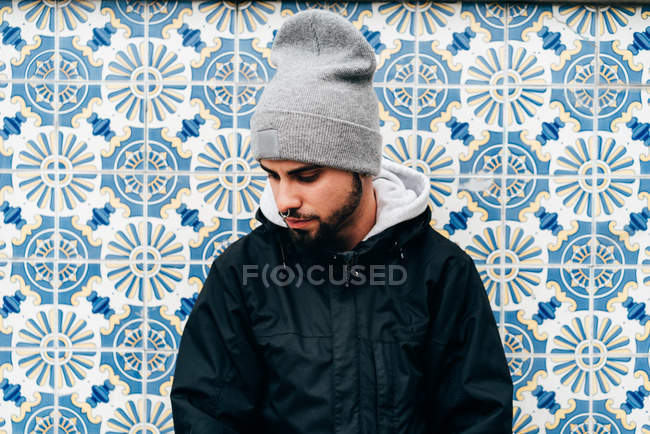 Retrato de turista masculino reflexivo de pie en la pared con azulejos azules - foto de stock