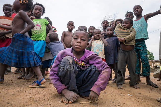 ANGOLA - ÁFRICA - 5 de abril de 2018 - Grupo de niños étnicos pobres y confiados sentados y parados en la calle de la aldea - foto de stock
