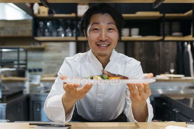 Lächelnder Koch zeigt Teller mit Essen im Restaurant — Stockfoto